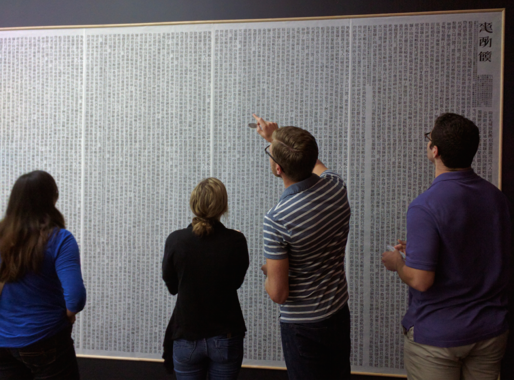 A photo of four people standing in front of scrolls featured in the 2016/17 exhibition Xu Bing: Book from the Sky at the Blanton Museum of Art, Austin, Texas