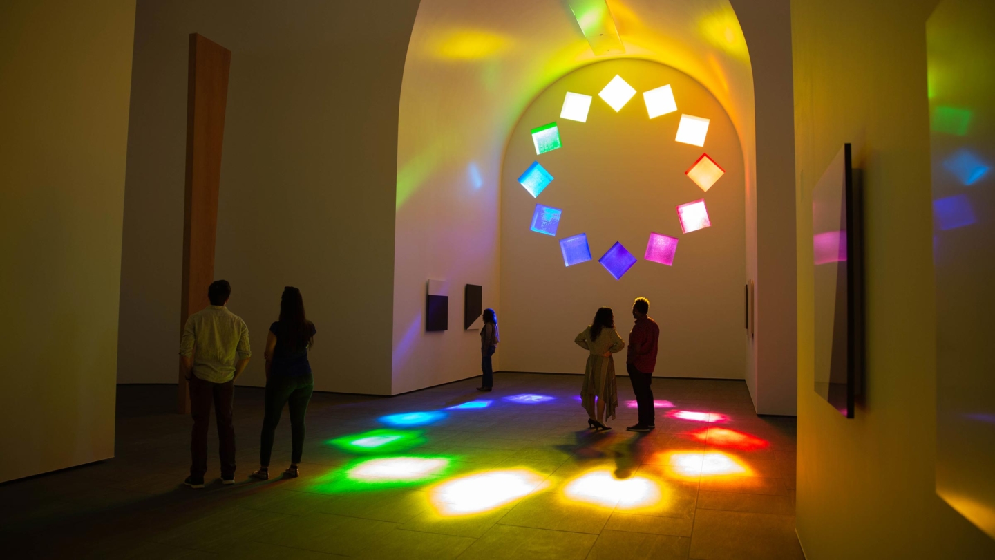 Five visitors admiring the rainbow shadows created by the stained glass windows inside of Austin by Ellsworth Kelly.