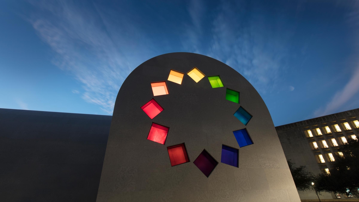 Evening view of the east wall of Ellsworth Kelly's Austin. The building is in shadow but the twelve stained glass square windows arranged in a circular pattern are brightly lit.