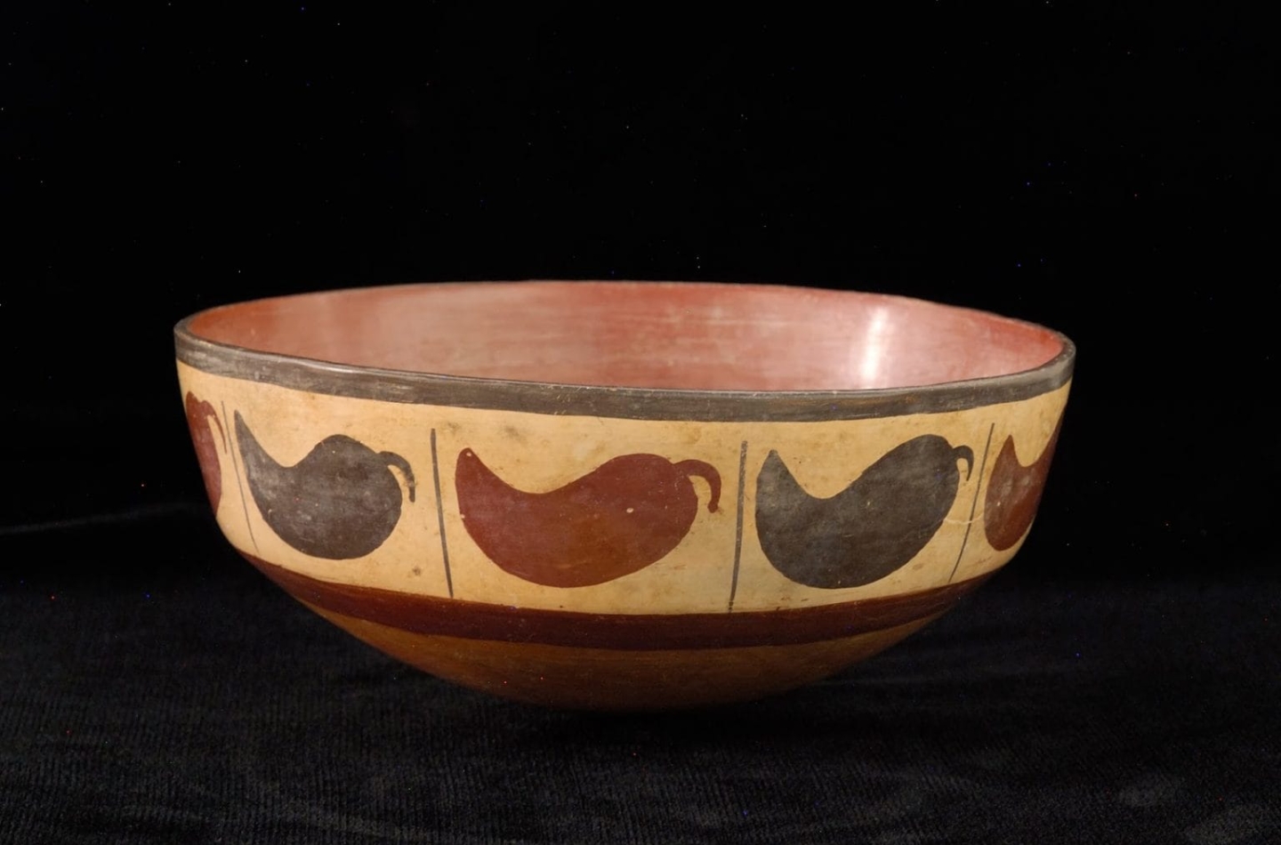 A ceramic bowl with chili peppers painted around the sides with varying shades of brown.