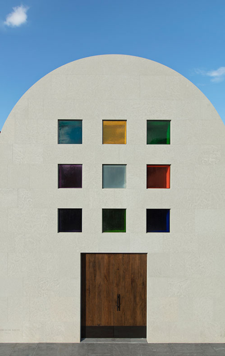 View of the entrance of Ellsworth Kelly's Austin with a blue sky above; nine rainbow squares make up a grid above two solid oak doors.