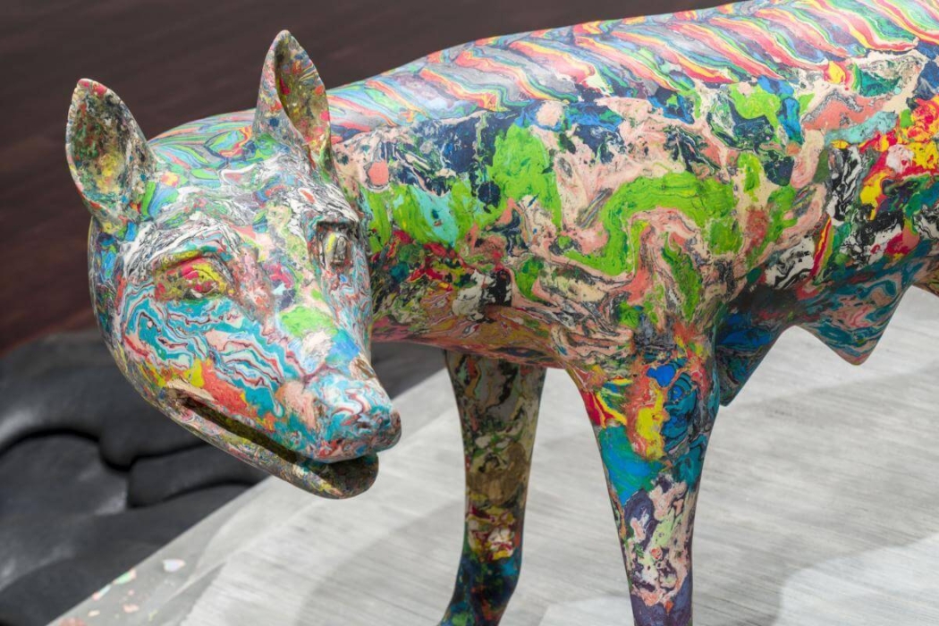 A colorful sculpture of an animal, likely a canine, with a vibrant and abstract paint pattern covering its entire body. The sculpture features a mix of bright colors including green, blue, pink, yellow, and red, creating a marbled effect. The animal is standing on a surface, and the detailed paintwork makes the sculpture visually striking and interesting.