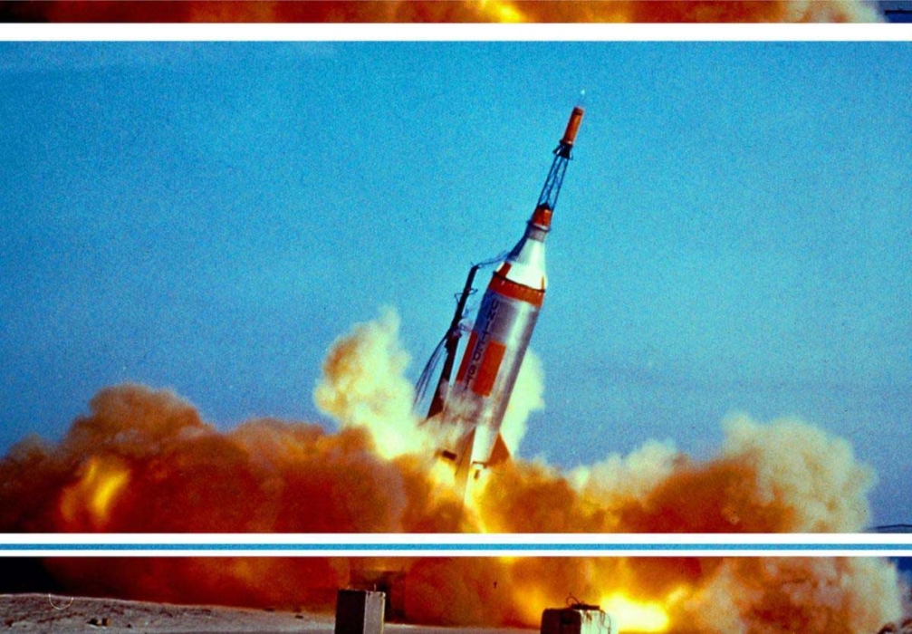 A rocket tilting at a steep angle mid-launch, surrounded by clouds of orange smoke and dust against a clear blue sky.