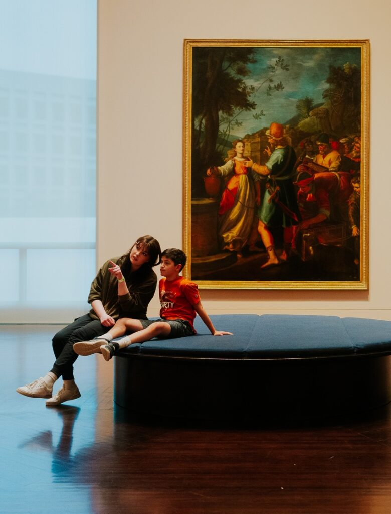 Mother and son sitting on a large, circular museum bench. In the background is a large scale painted artwork.