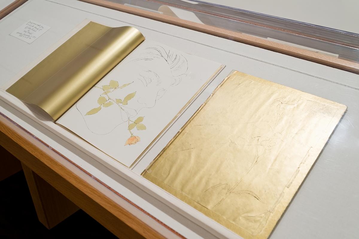 Printed books featuring illustrations using gold leaf embellishments in a display case.