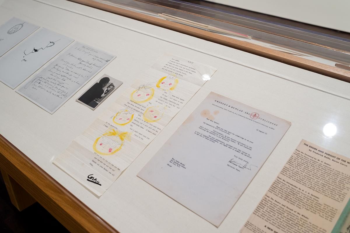 Prints and typed and handwritten letters in a display case.