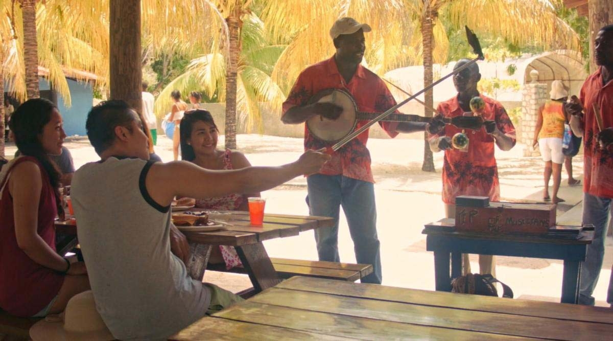 Individuals seated at tables listen to a man playing guitar, creating a vibrant and engaging environment.