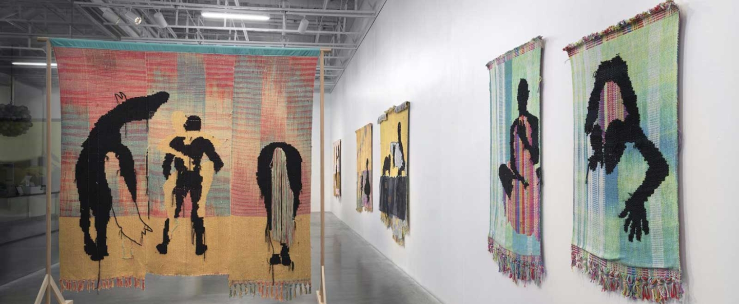 Art gallery featuring multiple tapestries featuring colorful backgrounds and black abstract figures.