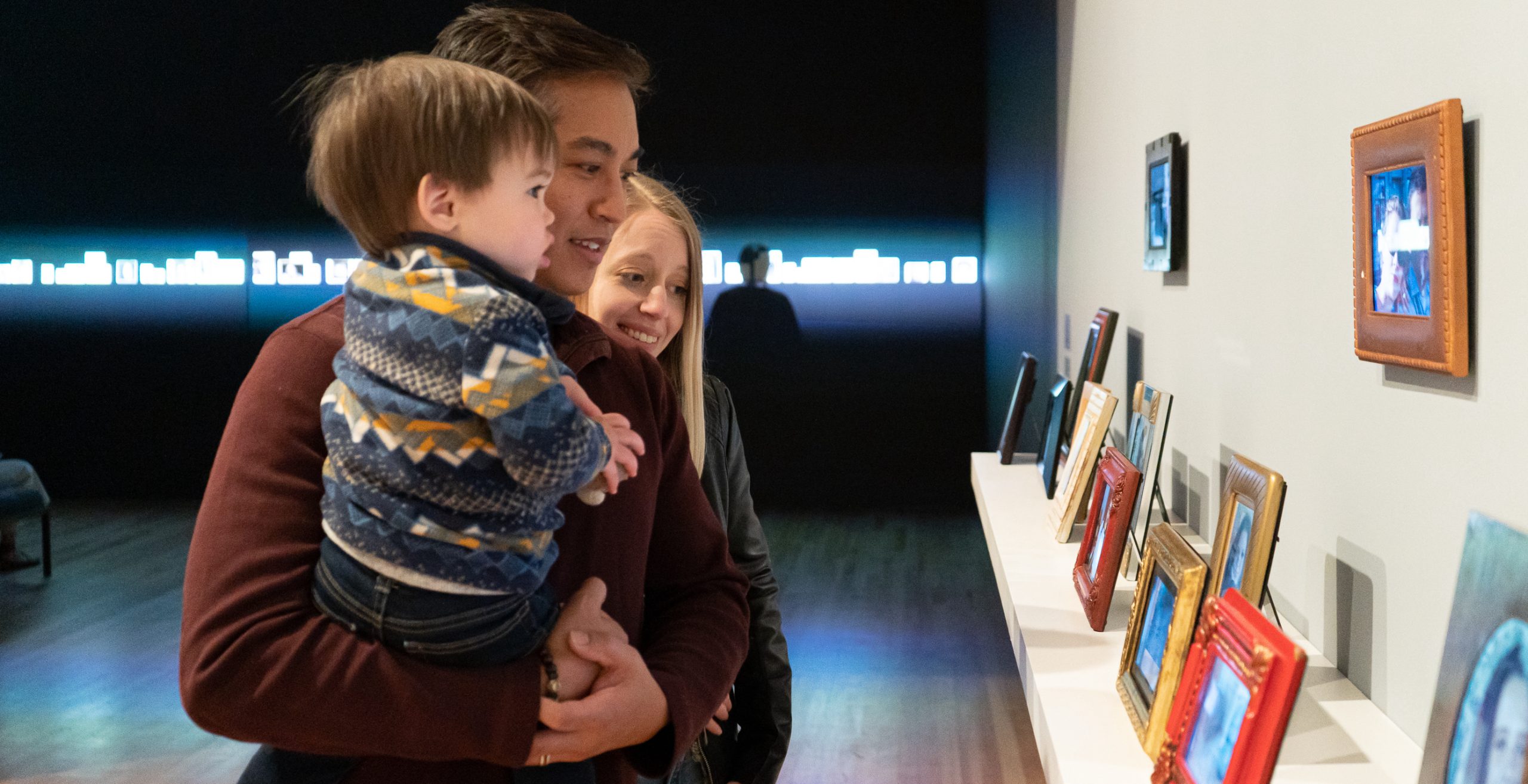 Side view of couple and their small child and viewing an artwork installation of picture frames.