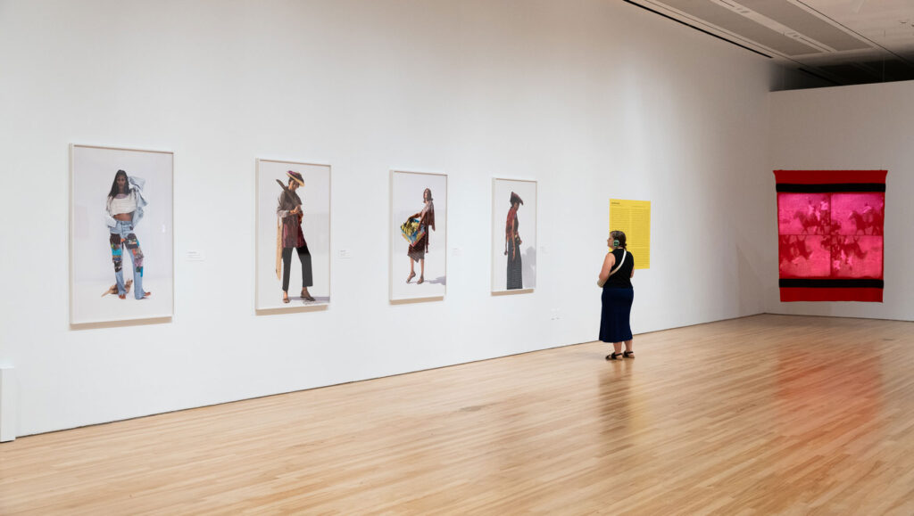 A gallery visitor wearing headphones looking at a wall of large scale photographs in an exhibition.