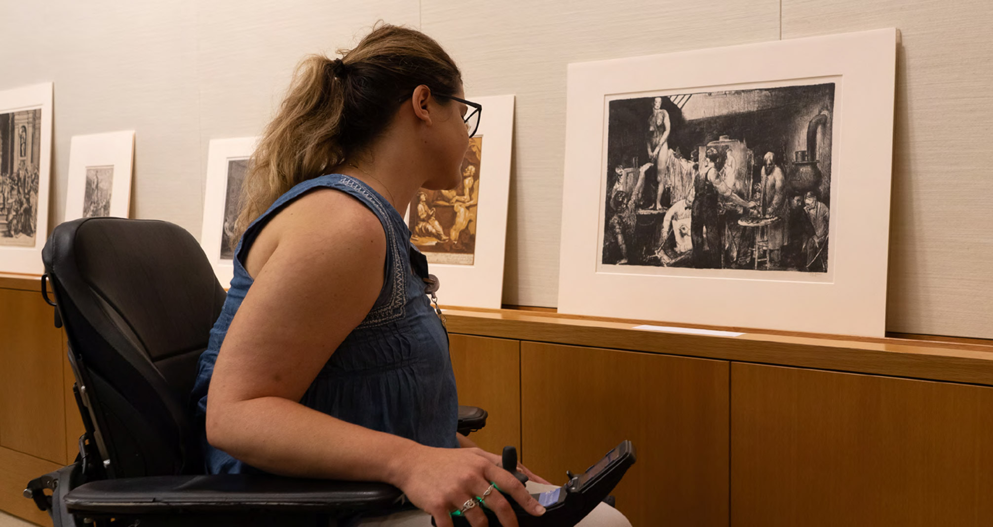 Visitor in a power wheelchair looking at artwork prints.